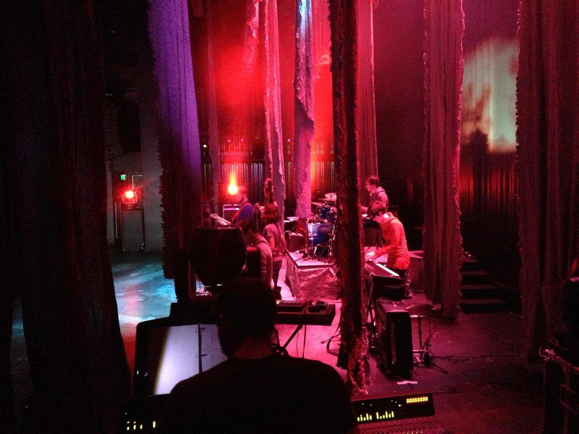 Medea — band framed by shredded curtains in deep red backstage light
