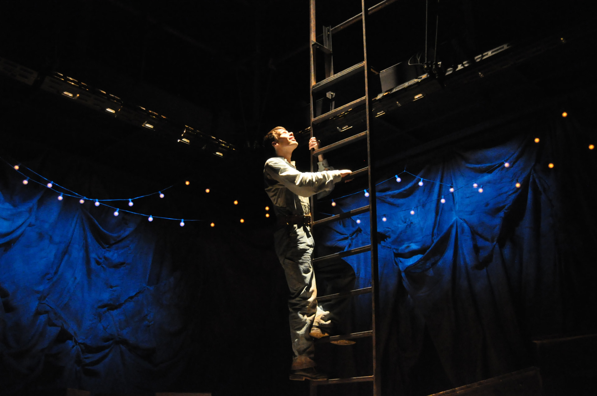 Floyd Collins — Homer climbing the ladder against the blue-lit drapes